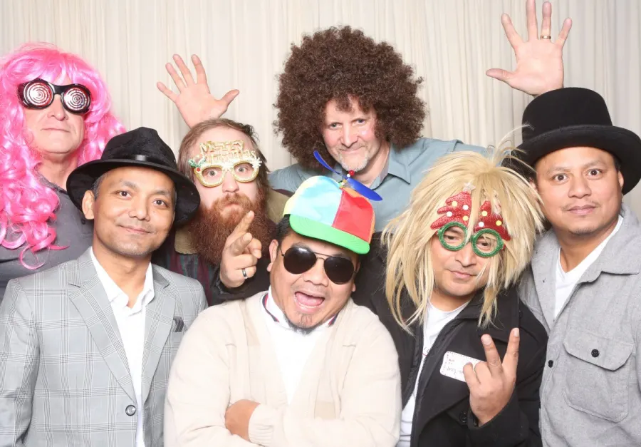 Big group in wigs, hats and novelty glasses at a party photo booth