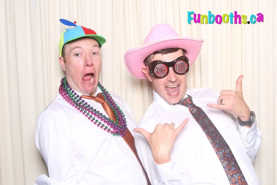 Two coworkers in a propeller hat and cowboy hat at an event photo booth