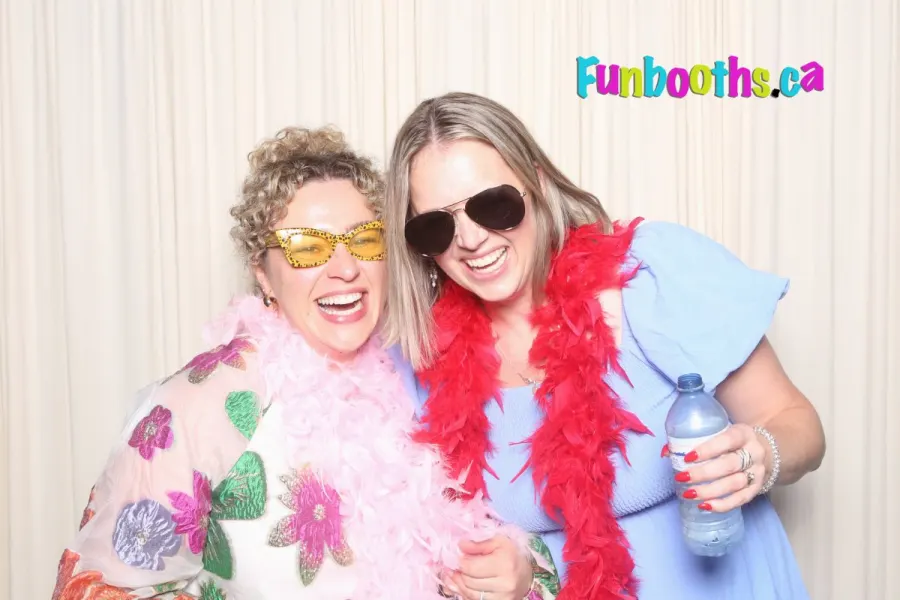 Two friends in feather boas and party glasses laughing in the photo booth