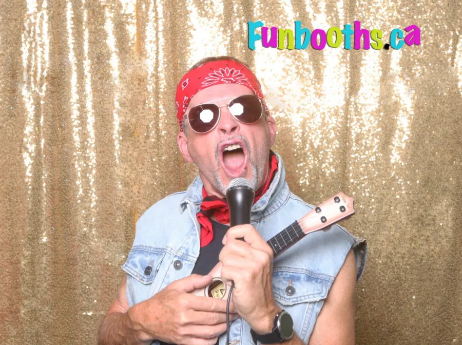 Guest singing into a prop microphone with a toy guitar in front of a gold backdrop
